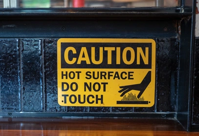 A yellow healthcare warning label stating "Hot Surface Do Not Touch," designed to prevent burns and ensure safety in medical or clinical environments.
